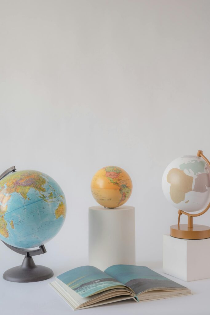 Three decorative globes and an open book on a minimalist white background.